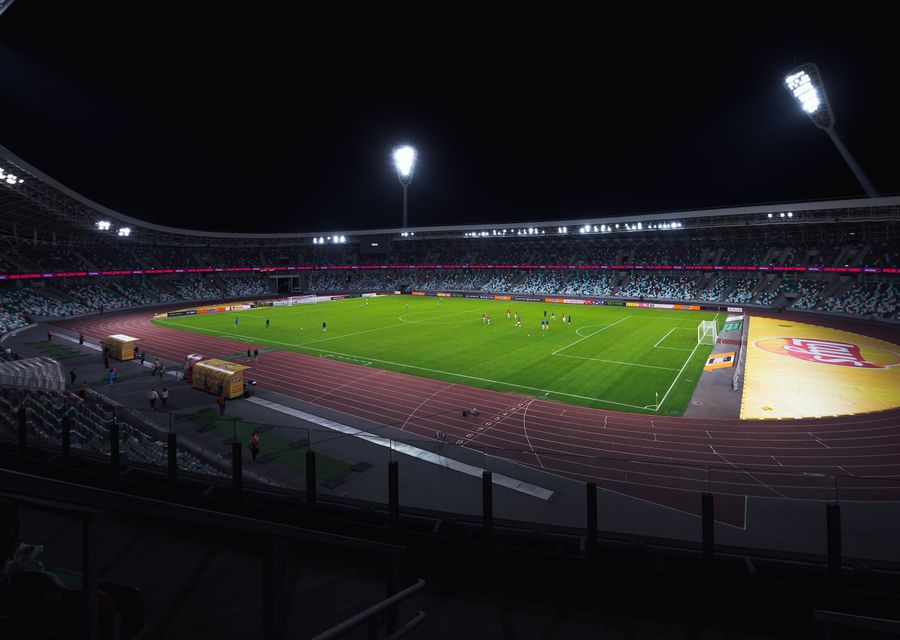 A floodlit sports ground at night, green field ringed by a running track